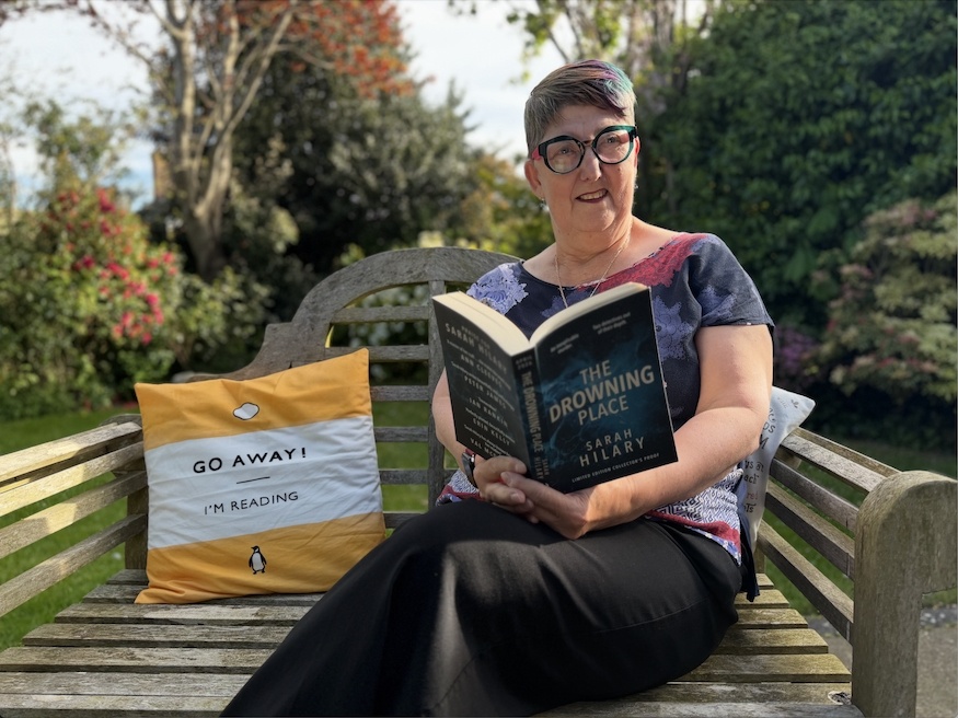Woman reading a crime novel on a bench for Crime Reading Month 2026