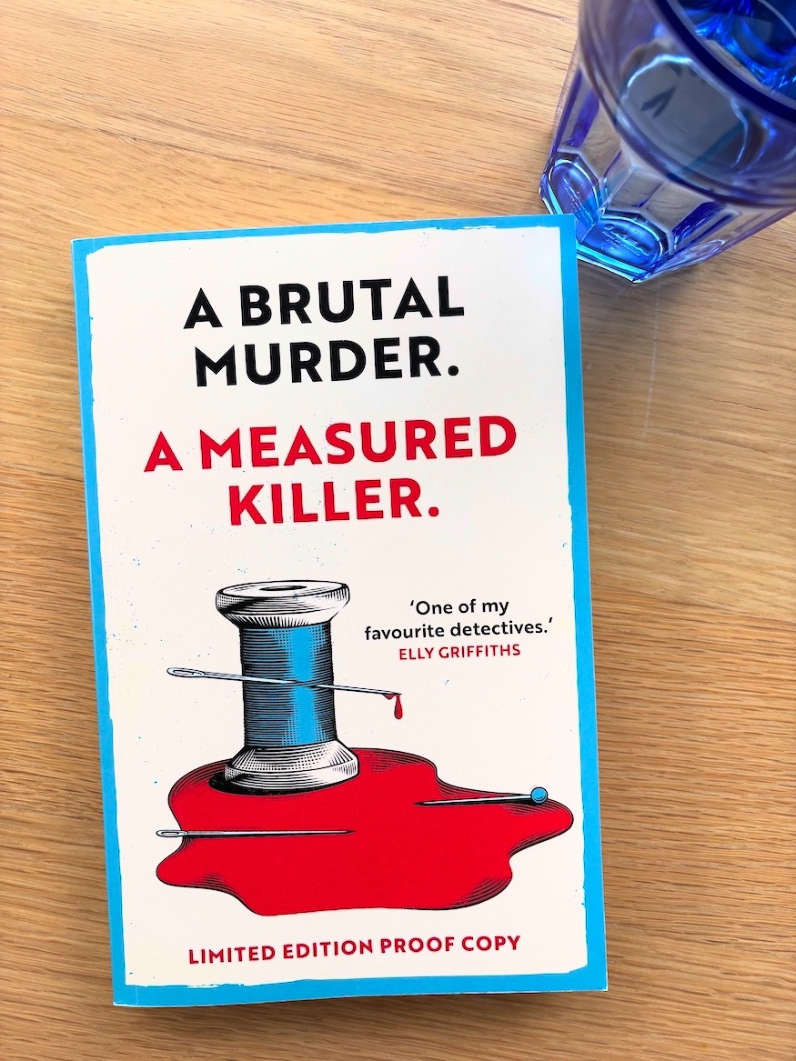 Advance reading copy of The Tailor by Tim Sullivan, on a table with a glass of water
